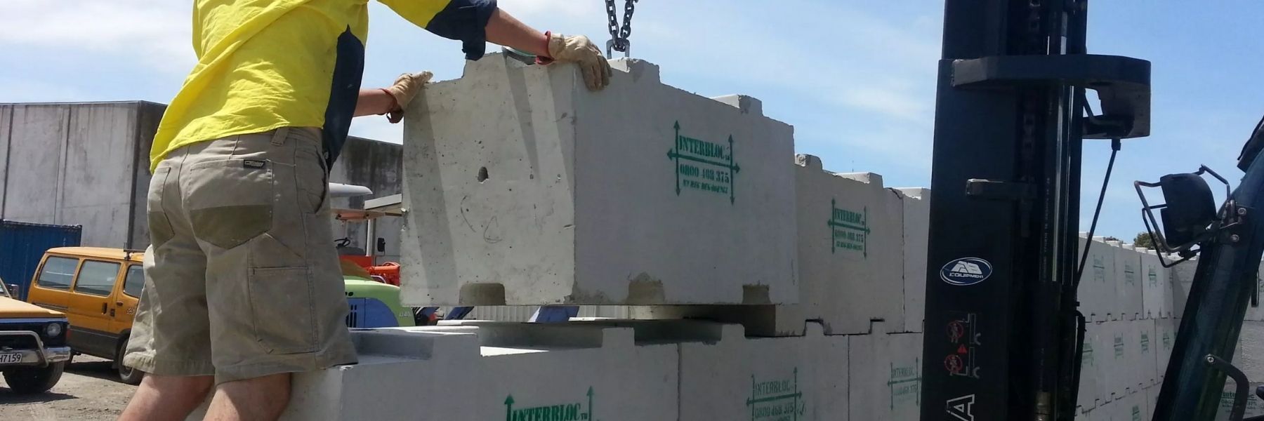 Worker installing a standard 1200 Interbloc concrete block on top of the already-built 2 rows underneath.