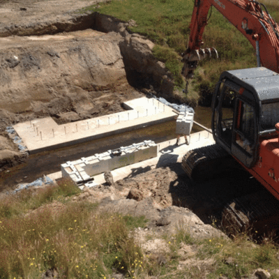 1200 Standard Interbloc concrete block being placed by a digger on the bottom layer of a culvert